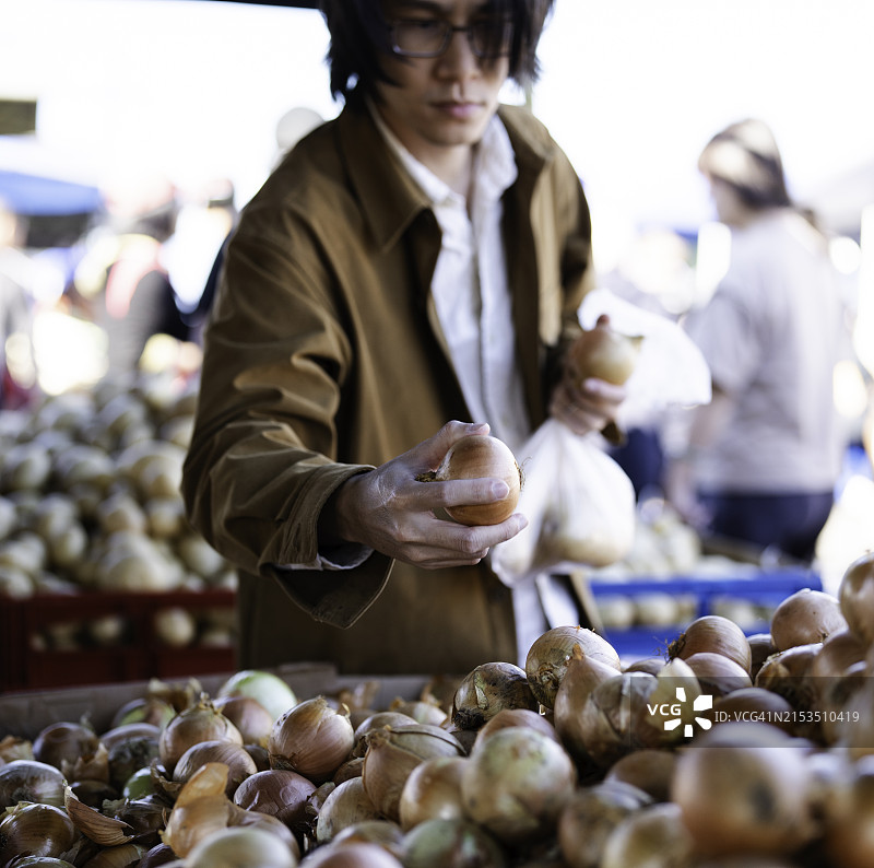亚洲男子在市场摊位挑选洋葱的特写图片素材