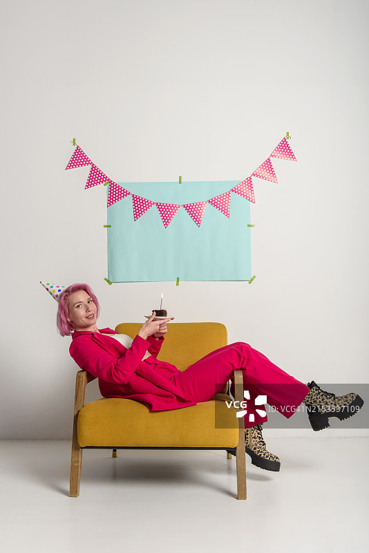 快乐的女人手捧生日蛋糕坐在椅子上摆姿势，摄影棚拍摄图片素材