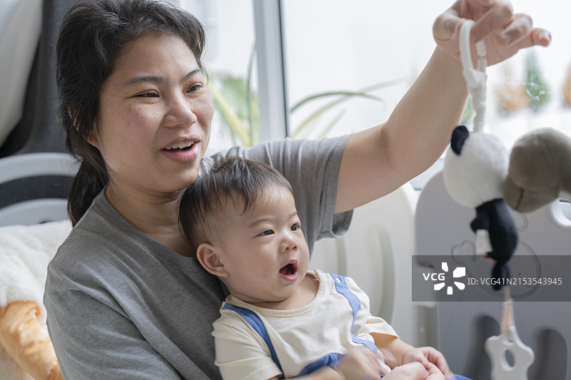 快乐的亚洲母亲与幼儿在婴儿床中玩耍，充满爱意和正能量图片素材
