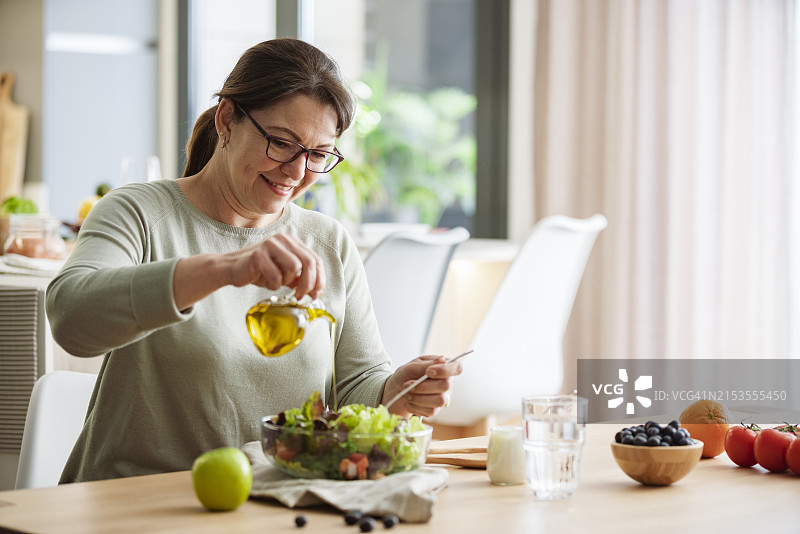 女人倒橄榄油在沙拉上，健康饮食和节食理念图片素材