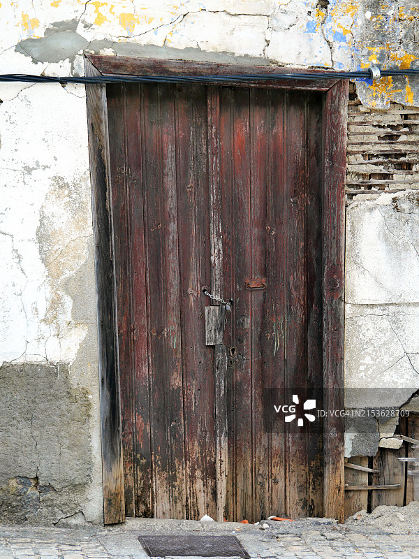 葡萄牙杜罗河谷皮尼奥，废弃房屋的风化木门和破裂的墙壁，阳光下的铺砌人行道图片素材