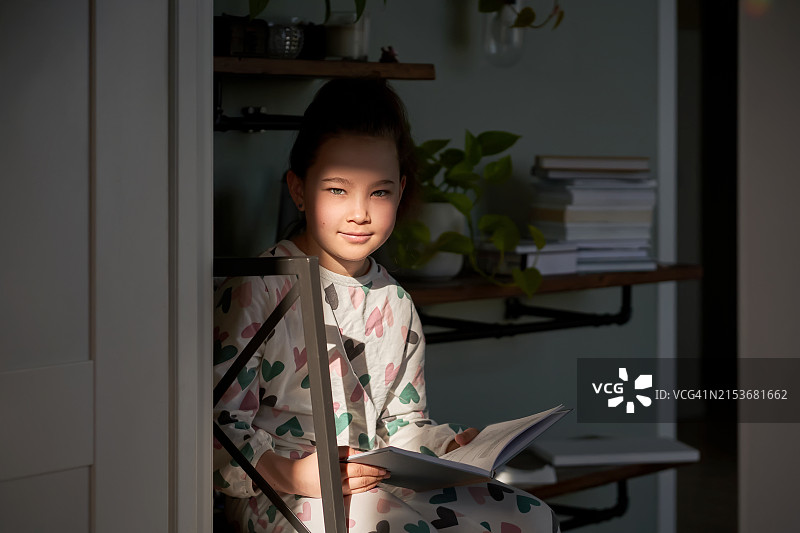 一个8岁的女孩穿着睡衣在阳光下读书图片素材