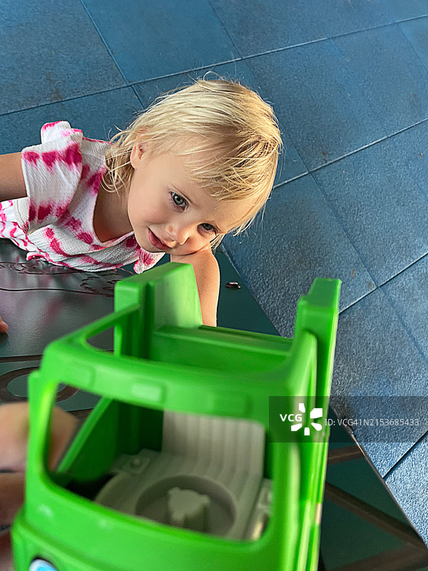 快乐的金发女宝宝在户外儿童乐园玩绿色玩具车图片素材