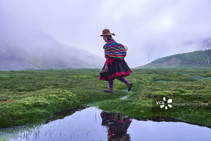 行走在安第斯山脉湖泊间的秘鲁盖丘亚族妇女和她的孩子图片素材