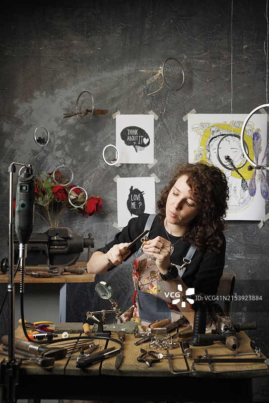 一位美丽的年轻女珠宝商正在制作一枚手工戒指，她正在使用金属锉刀。珠宝工匠工作坊图片素材