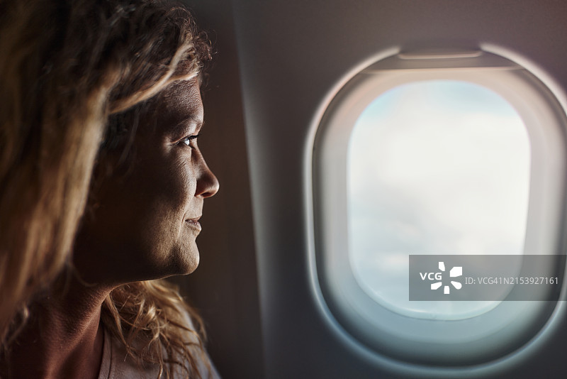笑容满面的女人在飞机上旅行时做白日梦图片素材