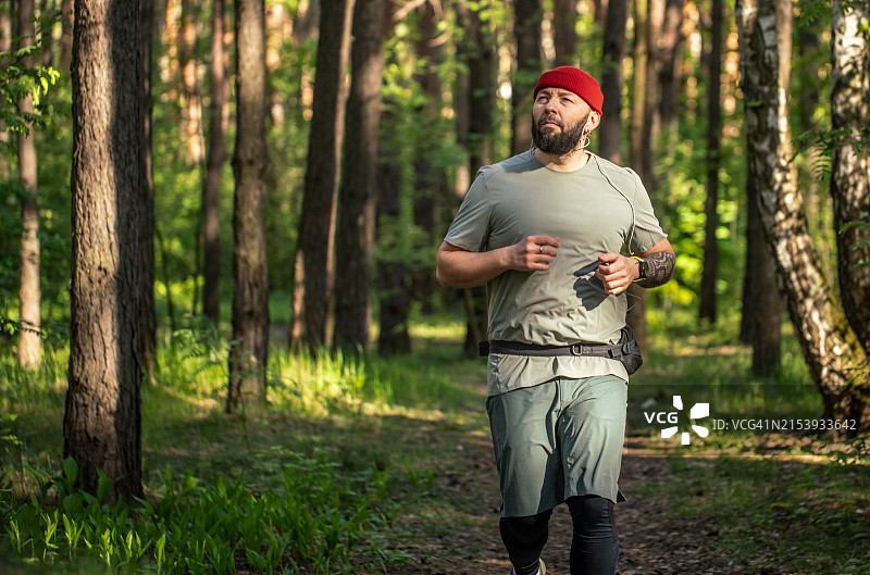 在森林中慢跑。男人在森林中的人行道上跑步，早上戴着入耳式耳机听音乐图片素材