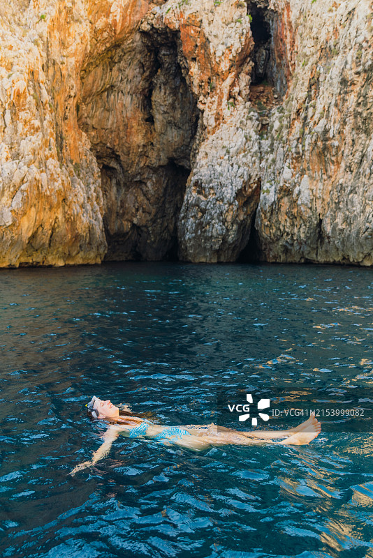 戴着水肺面罩在水晶般蓝色水域洞穴内游泳的快乐女人图片素材