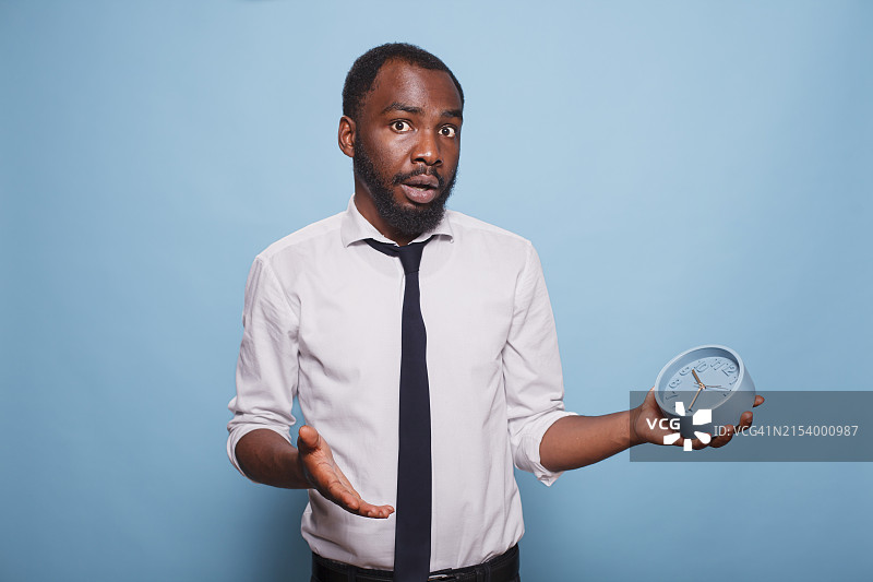 在蓝色背景下手持时钟的商务人士肖像图片素材