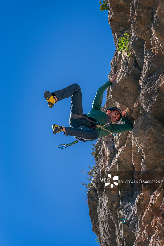 仰视角度：男人在晴朗的蓝天下攀岩图片素材