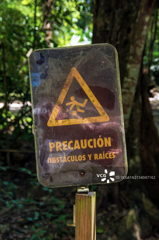 危地马拉蒂卡尔考古遗址的西班牙语警告标志，上面写着“Precaución: Obstáculos y raíces”[注意：障碍物和树根]图片素材