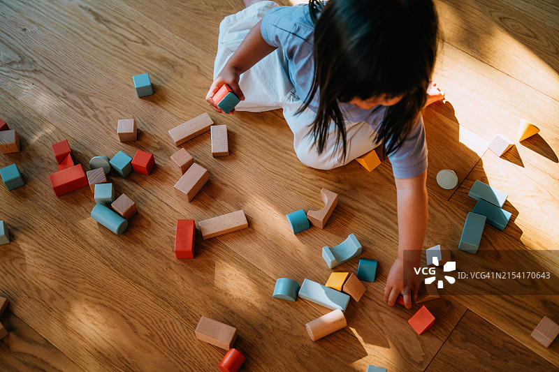 俯视：亚洲幼儿女孩在木地板上玩积木图片素材