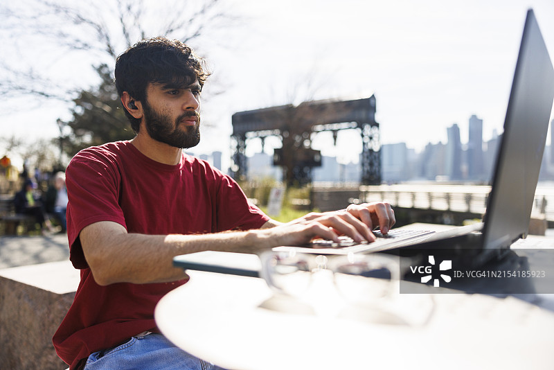 公园里的工作生活平衡：巴基斯坦男子在户外使用笔记本电脑和耳机通话图片素材