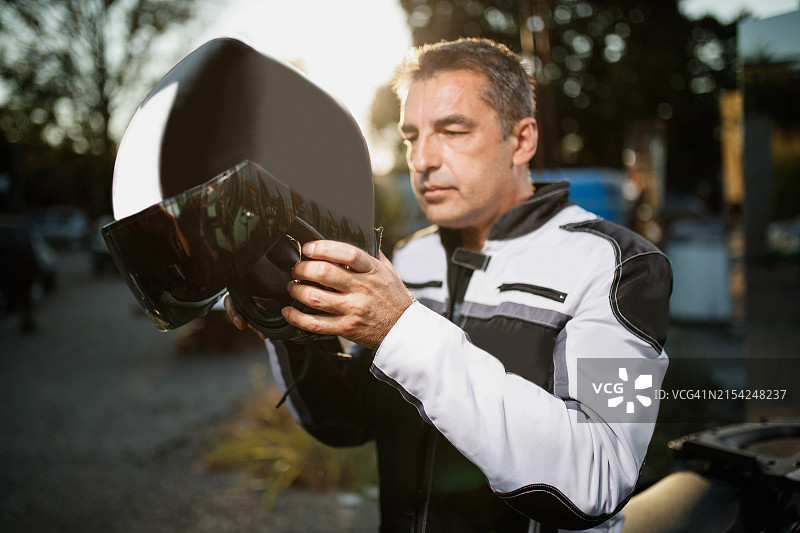 黎明时分，穿着机车夹克的成熟男人在骑行前拿着自行车头盔图片素材