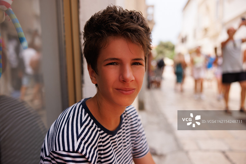 坐在海边石板路商店橱窗旁的少年图片素材