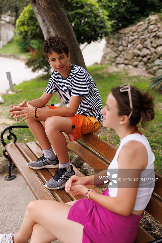 少女和弟弟坐在公园长椅上，在海边小镇享受夏日时光图片素材