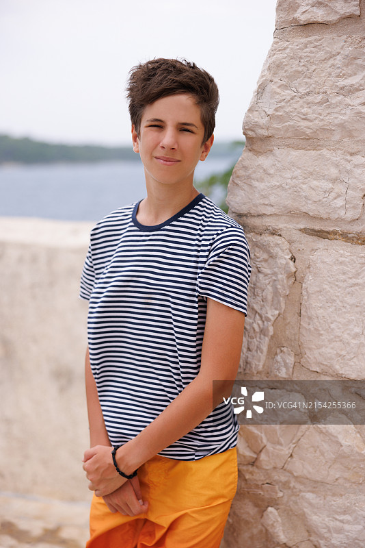 在海边石墙观景点享受夏日的可爱少年图片素材