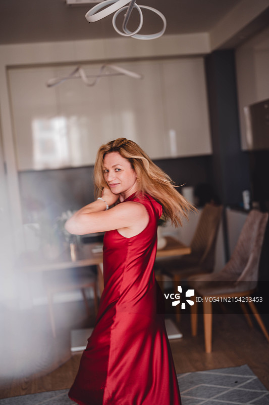 一位穿着红色连衣裙的漂亮女人在她的公寓里跳舞。图片素材