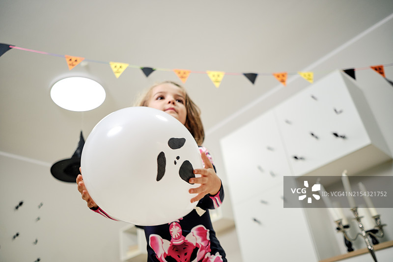 小女孩打扮成骷髅，在客厅里拿着一个鬼脸气球图片素材