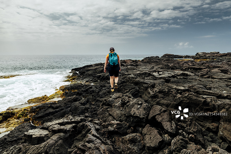 女人在夏威夷大岛海岸边的火山岩上行走图片素材
