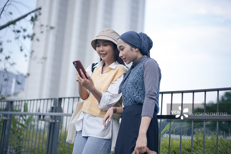 两名戴帽子头巾的年轻女人在户外看手机图片素材