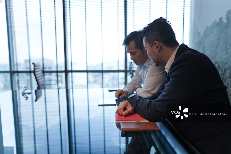 在现代办公室玻璃会议桌旁进行严肃讨论的两位商人图片素材