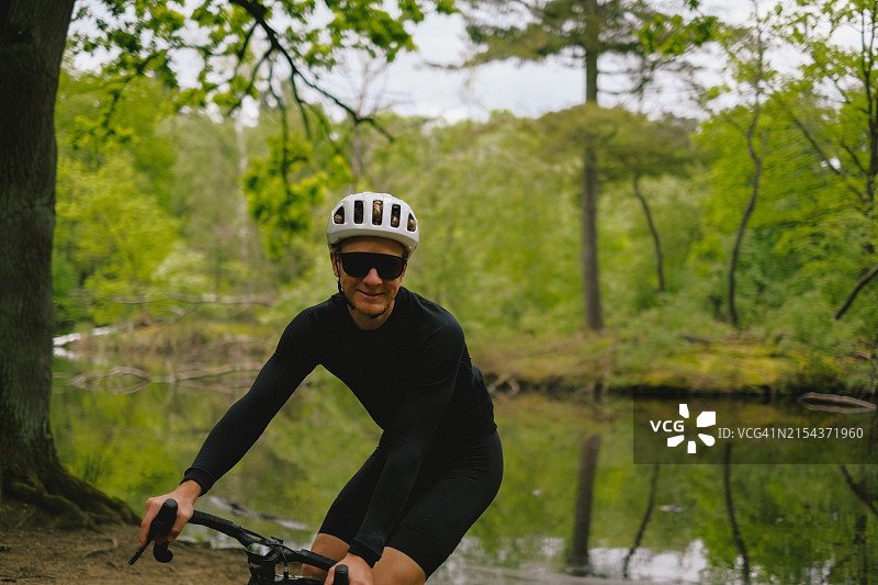 骑自行车者沿森林中的湖泊旁的道路骑行图片素材
