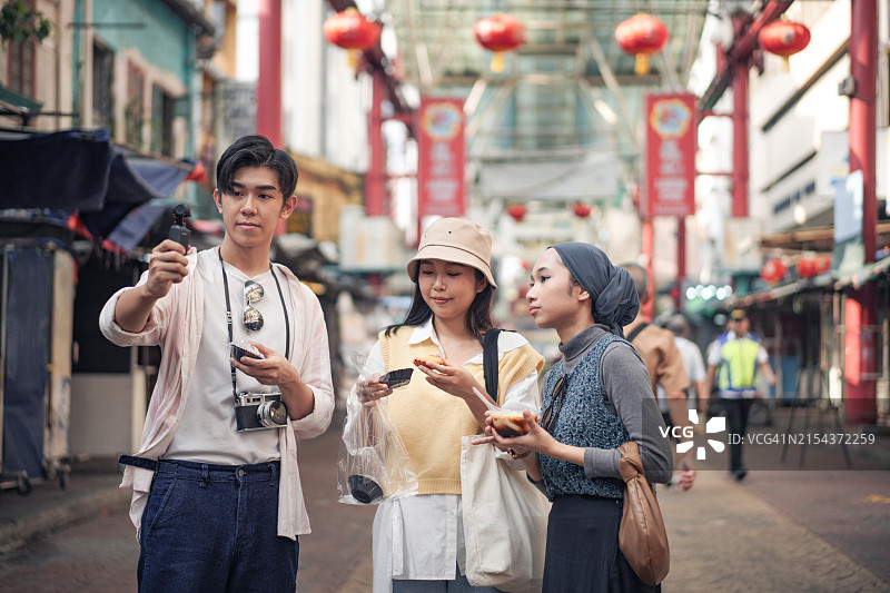朋友们在热闹的户外市场享用街头美食，分享美食，笑容满面图片素材