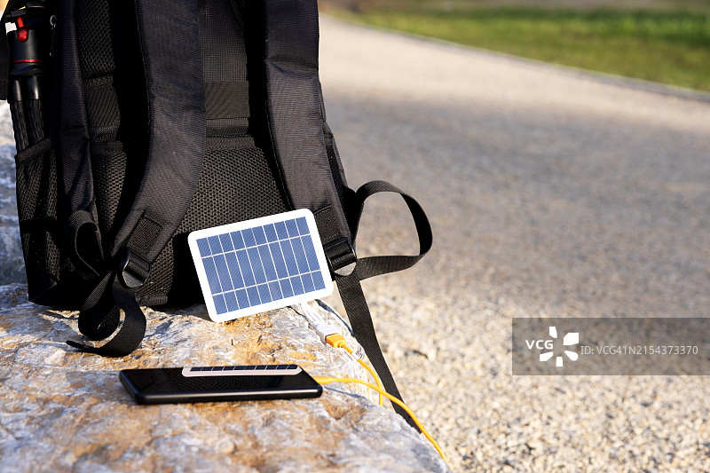 智能手机放在大石头上，连接到背包上的太阳能电池板图片素材