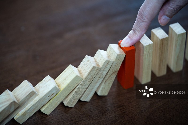 商务女性之手阻止多米诺骨牌倒塌，商业危机管理概念图片素材