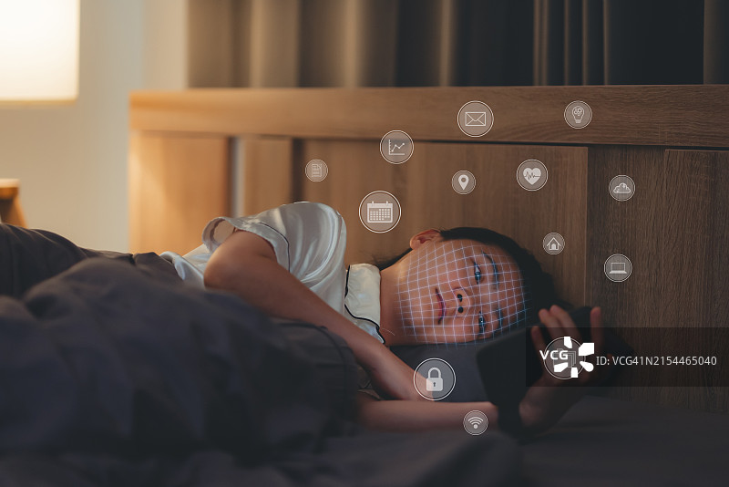 亚洲女人晚上在卧室用智能手机扫描面部ID。图片素材