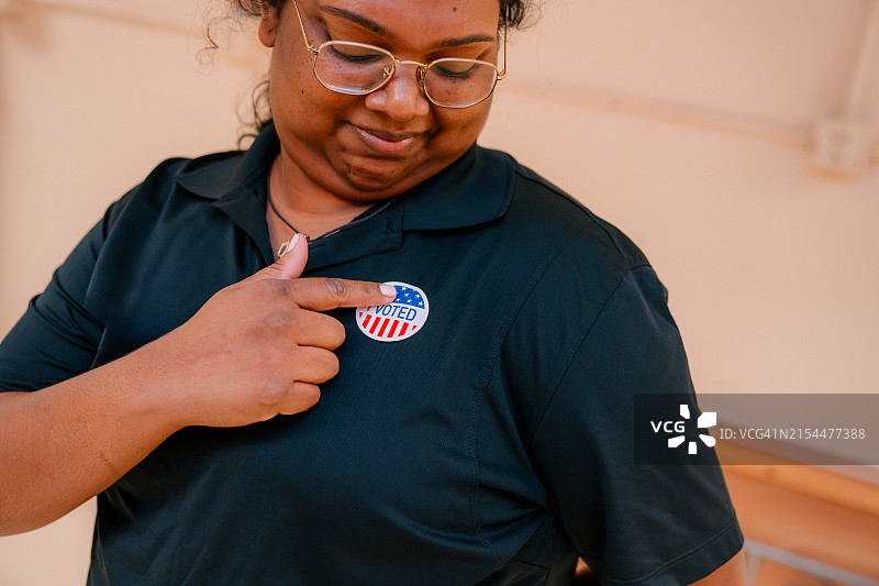 居住在美国佛罗里达州的特立尼达裔美国年轻移民妇女，指向室内“我已投票”贴纸图片素材