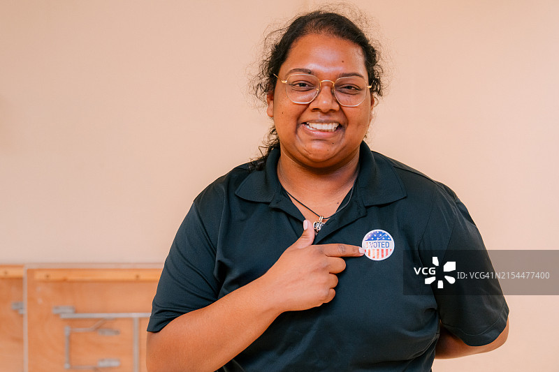 快乐的特立尼达裔美国移民年轻女性，美国佛罗里达州居民，指向室内“我投票了”贴纸图片素材