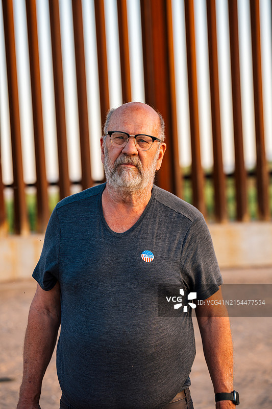 站在美国-墨西哥边境墙旁，贴着“我已投票”贴纸的男人肖像图片素材