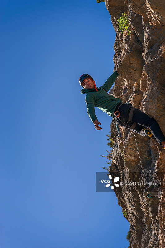 仰视角度：男人在晴朗的蓝天下攀岩图片素材