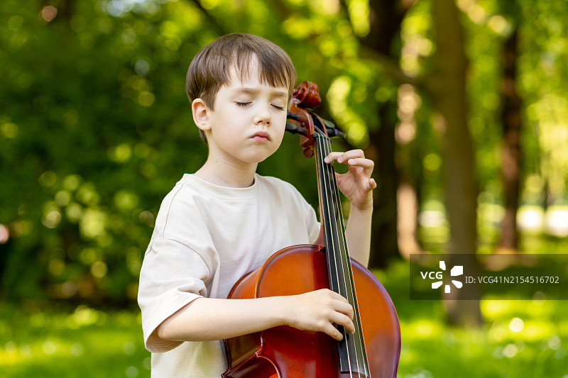夏天在户外演奏大提琴的6岁男孩肖像图片素材