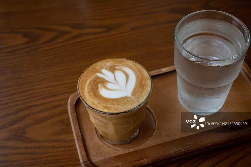 咖啡杯特写，含拿铁拉花和一杯木托盘上的水图片素材