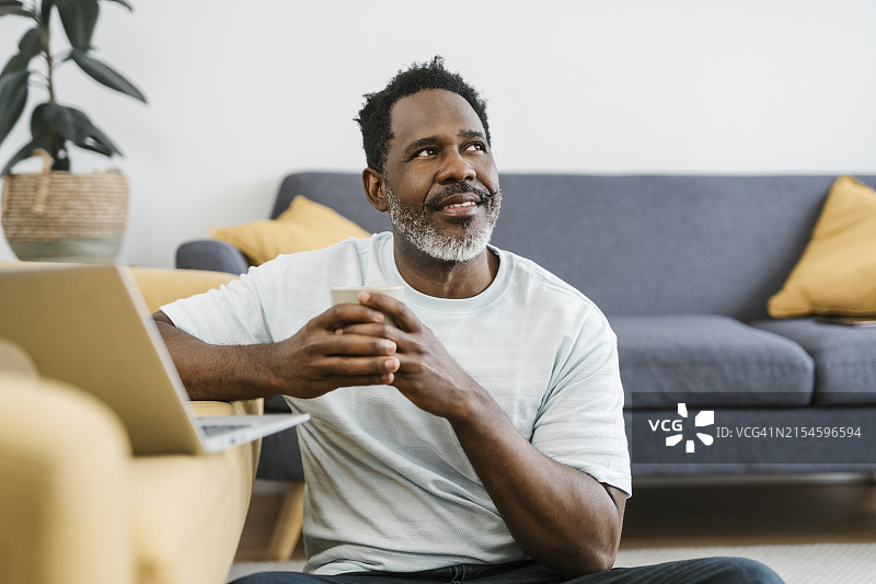 在家喝咖啡并使用笔记本电脑的分心中年非洲男人图片素材