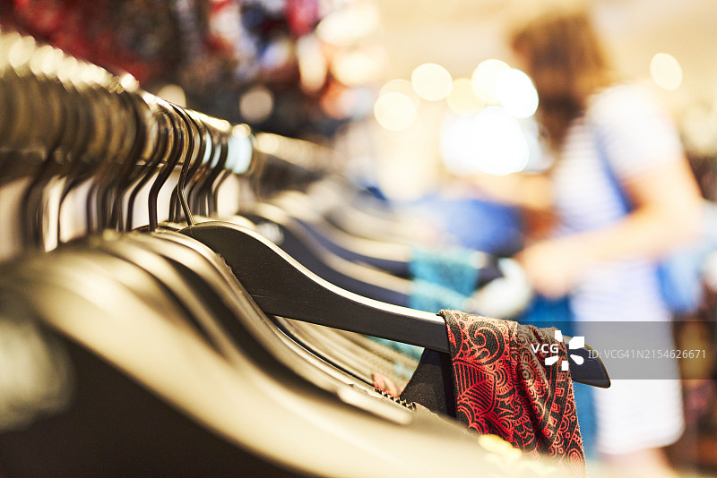 挂满一排连衣裙的衣架正面特写，背景中有一名女子图片素材