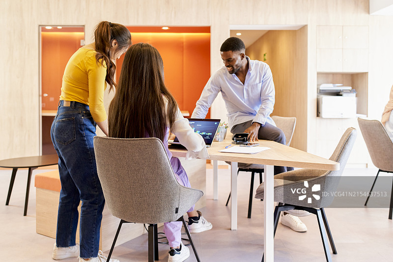不同种族的同事聚集在办公室，桌上放着一台笔记本电脑图片素材