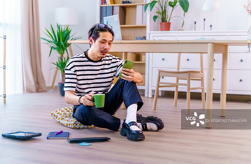 身穿条纹T恤的年轻男子正在使用手机和咖啡杯浏览社交媒体图片素材