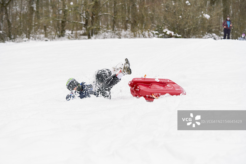 从红色雪橇上摔下来的男孩图片素材