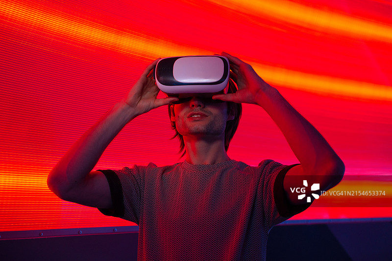 戴着VR眼镜，站在红色霓虹灯墙前的未来主义男子图片素材