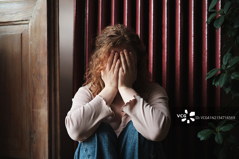 坐在地上，用手捂着脸，感到沮丧和失望的青少年；在家哭泣的女人。青春期抑郁症图片素材