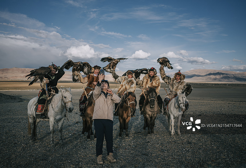 快乐的中国女性游客在巴彦乌列盖与骑马的哈萨克猎鹰人合影图片素材