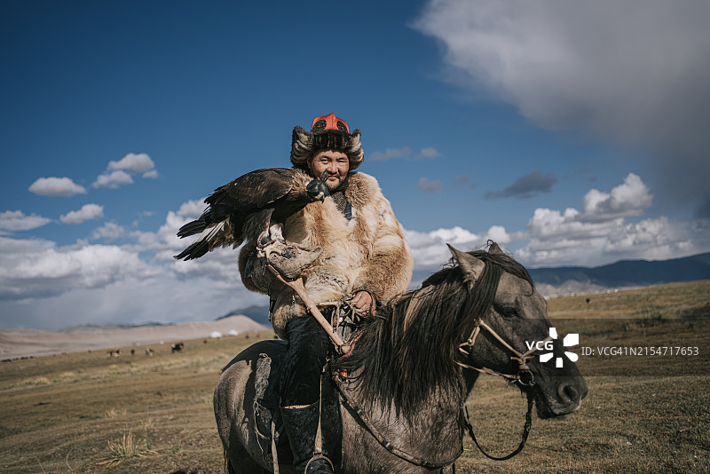 自豪的哈萨克族猎鹰人骑在马背上看着镜头微笑，巴彦乌列盖，蒙古西部图片素材