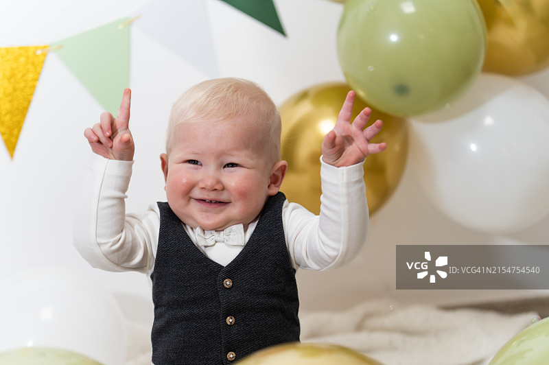 可爱的男婴玩耍，坐在气球旁举起手臂图片素材