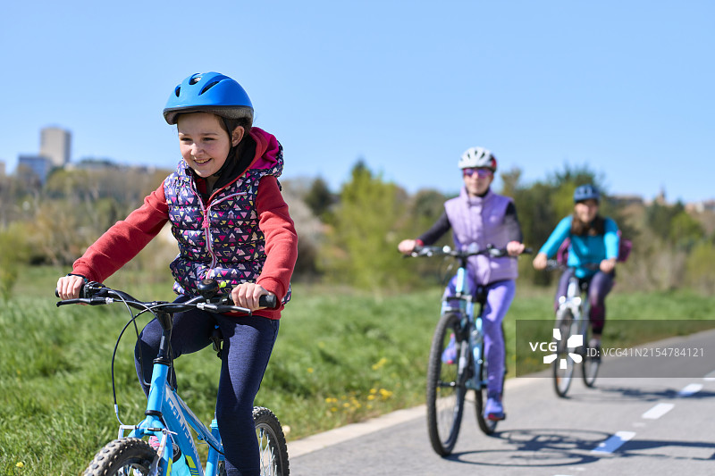 女孩们在保护装备中骑自行车比赛，母亲在背景中，正面视角图片素材