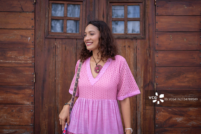穿着粉红色连衣裙，在乡村木门旁摆姿势的微笑女人图片素材
