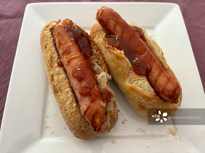 盘子里两根脆皮面包卷热狗配酸菜番茄酱图片素材
